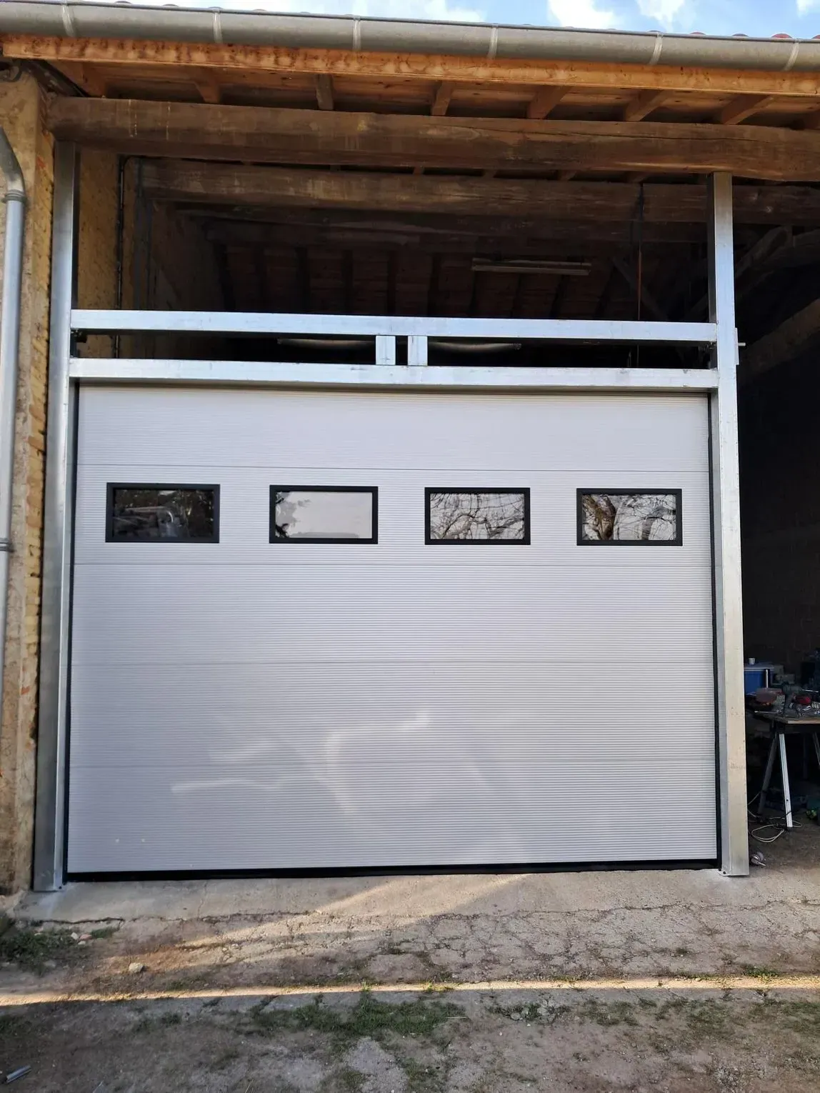 Porte de garage blanche avec quatre petites fenêtres sous un abri de voiture en bois.