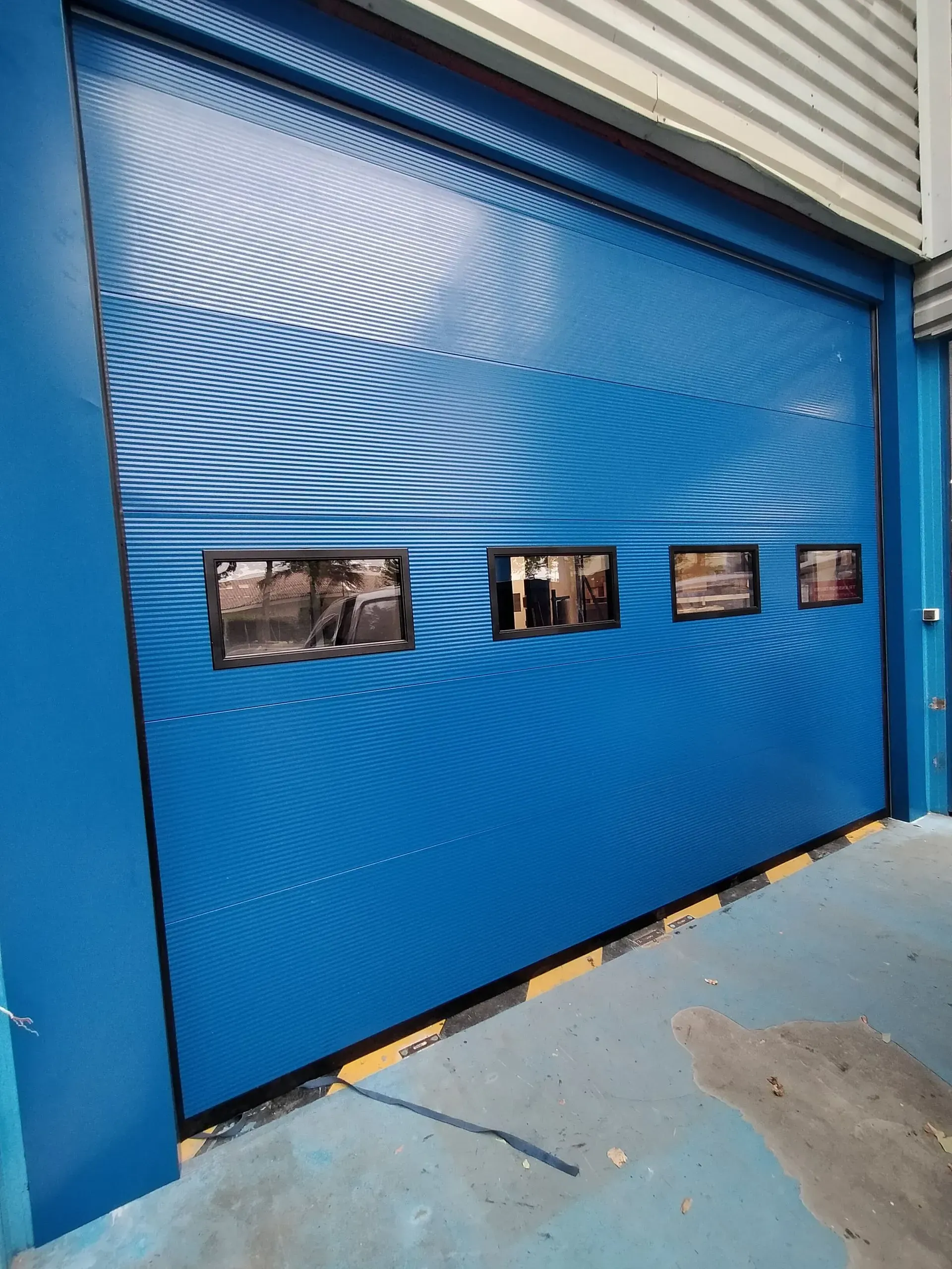 Porte sectionnelle industrielle bleue avec quatre petites fenêtres en bas de l'entrée d'un entrepôt.