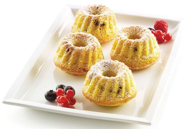 Ein weißer Teller, belegt mit vier Mini-Gugelhupfen und Beeren.