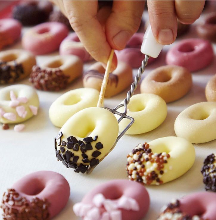 Eine Person taucht einen gelben Donut in Schokolade