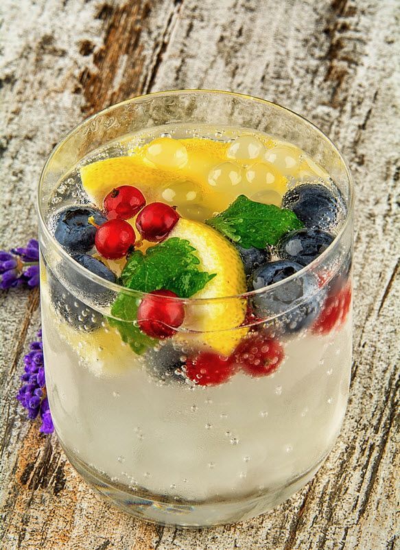 Ein Glas Wasser mit Zitrone, Blaubeeren und Preiselbeeren auf einem Holztisch.