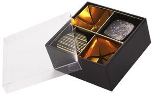 Eine schwarze Schachtel mit vier Stück Schokolade darin und einem durchsichtigen Deckel.