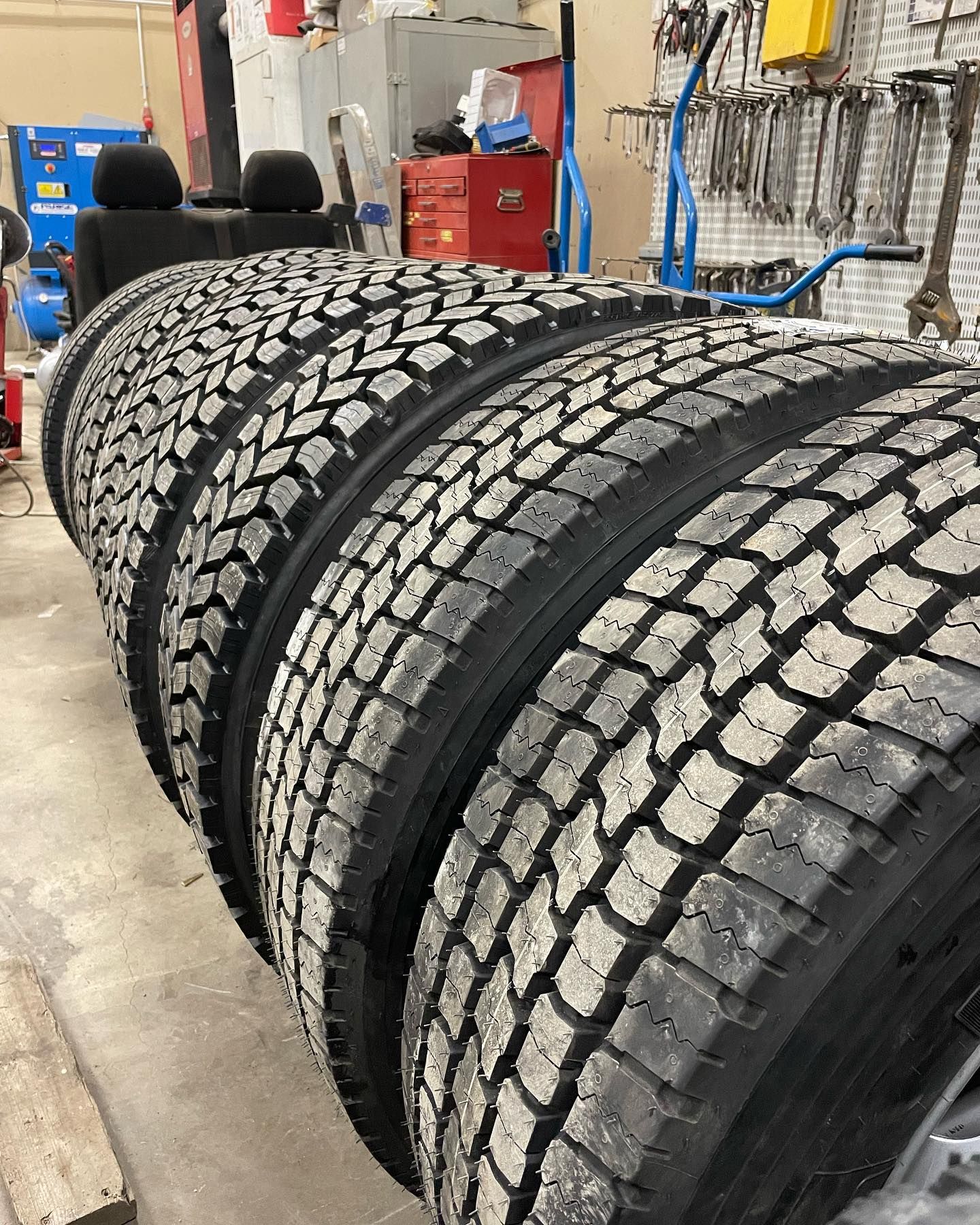 Neljä kuorma-auton rengasta rivissä, kulutuspintakuviot näkyvissä, korjaamon sisällä.