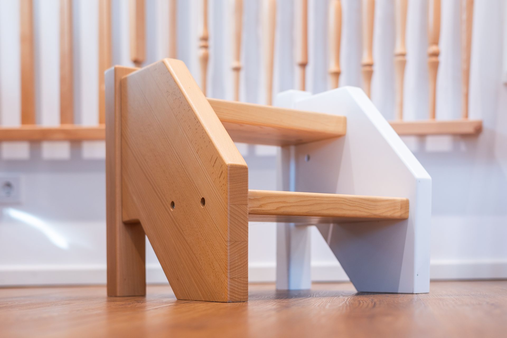 Ein hölzerner Tritthocker steht auf einem Holzboden neben einer Treppe.