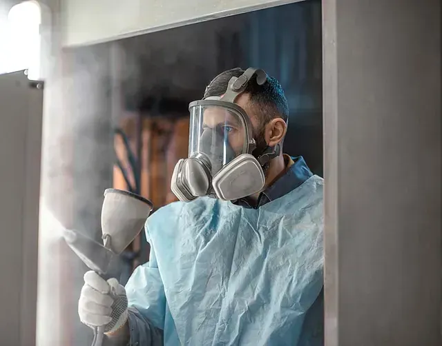 Una persona con un traje protector y una máscara respiratoria rocía una superficie con una pistola de pintura.