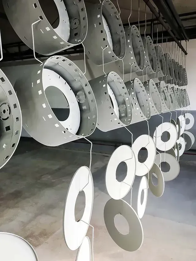 Componentes metálicos de color gris claro de una lámpara cuelgan de cables en un tendedero en un entorno industrial.