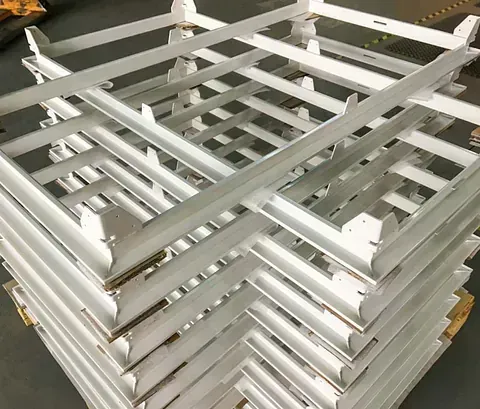 Una pila de marcos o paletas industriales de metal blanco y rectangulares que descansan sobre una base de madera en un taller.