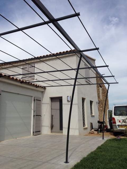 Une pergola en métal installée au-dessus d'une allée pavée devant une maison avec garage.