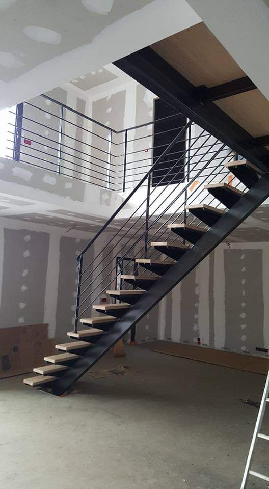 Un escalier industriel moderne, avec une structure en métal et des marches en bois, est en construction dans une pièce aux cloisons sèches apparentes.