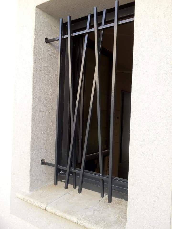 Une fenêtre dotée de barreaux de sécurité en métal disposés selon un motif géométrique unique et non parallèle.