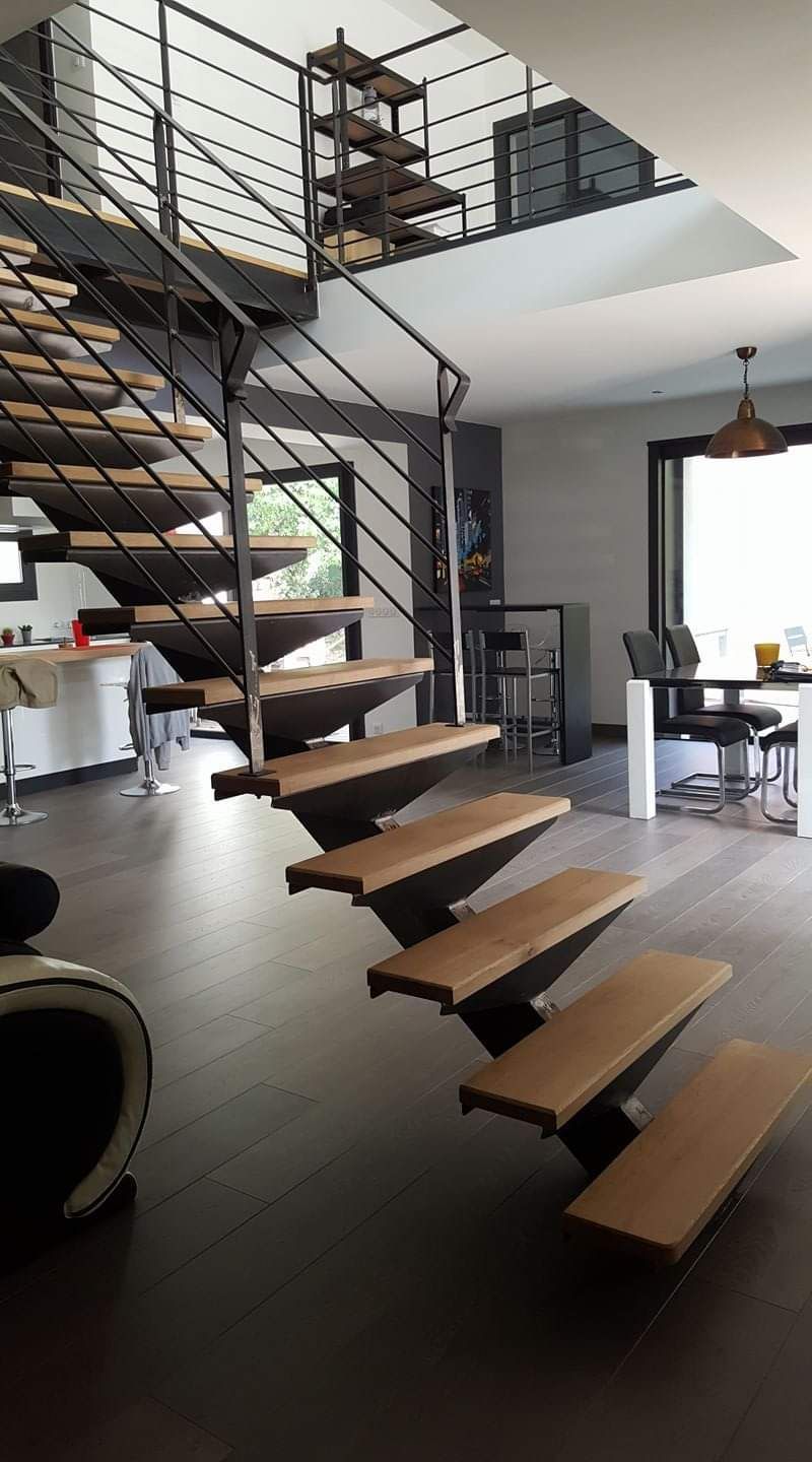 Un salon moderne est doté d'un escalier en bois ouvert et suspendu, avec des rampes en métal, menant à un palier supérieur.