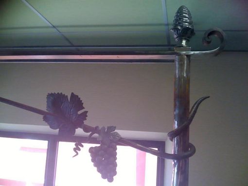 Objet décoratif en métal représentant une vigne sculptée, avec des feuilles et des fruits enroulés autour d'un poteau surmonté d'un fleuron.
