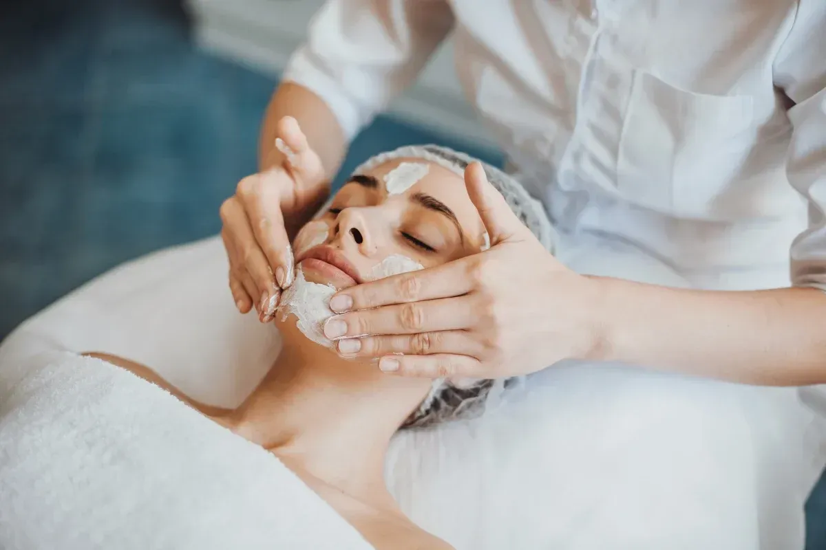 Mujer recibiendo tratamiento facial en un spa, aplicando crema en las manos.