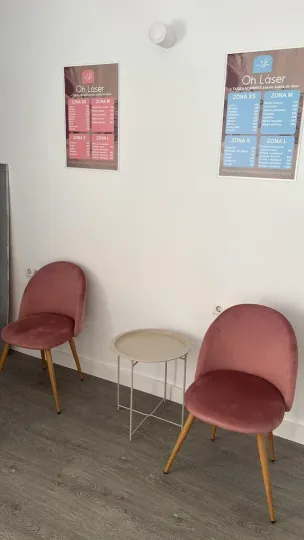 Dos sillas rosas, mesa pequeña, carteles sobre pared blanca.