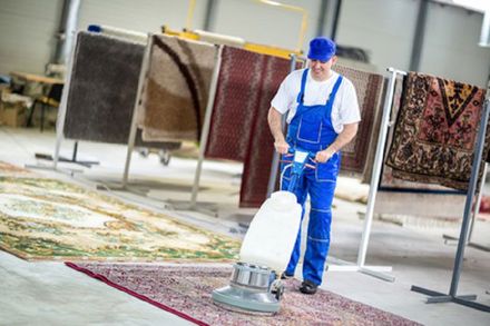 Ein Mann reinigt in einer Lagerhalle einen Teppich mit einer Maschine.