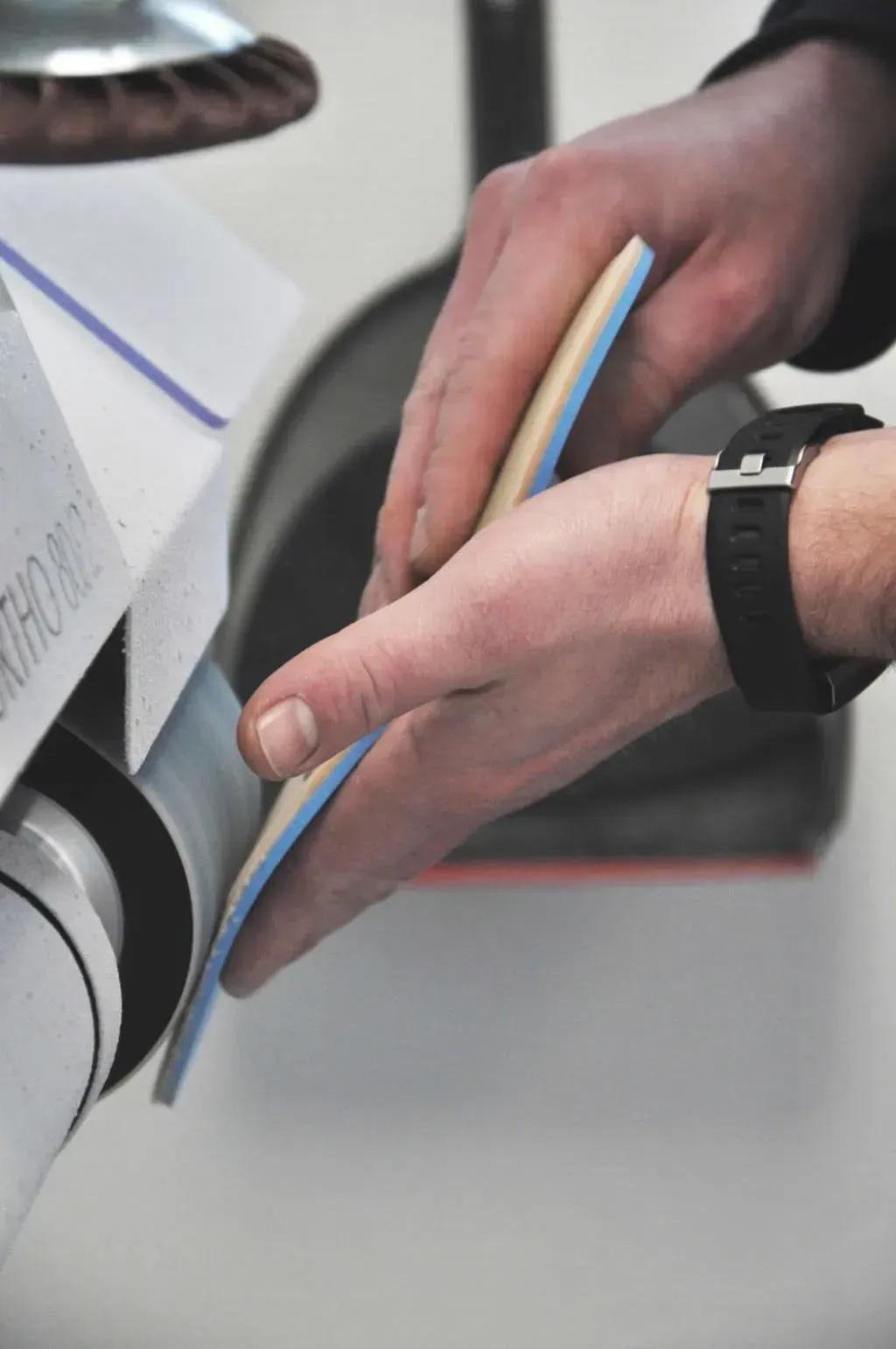 Eine Person formt mit einer Schleifmaschine eine Einlegesohle. Die Hände sind sichtbar.