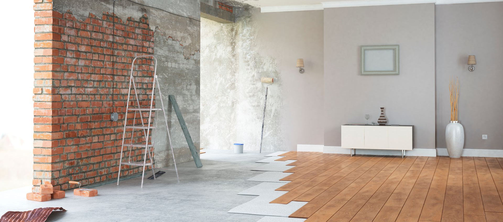 Une pièce en rénovation avec un mur de briques partiellement apparent, une échelle et une transition entre le sol en béton et le sol en bois.