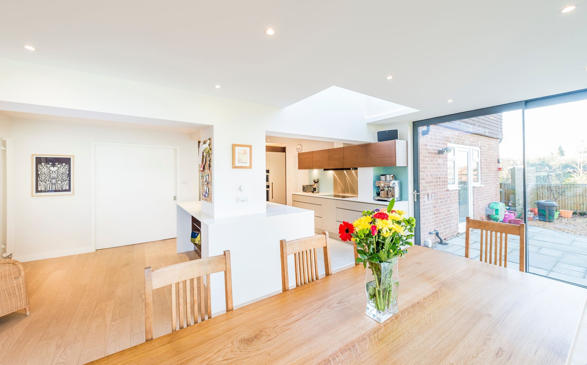 Une cuisine et une salle à manger modernes et ouvertes, avec une table en bois ornée de fleurs et des portes coulissantes en verre donnant sur une terrasse.