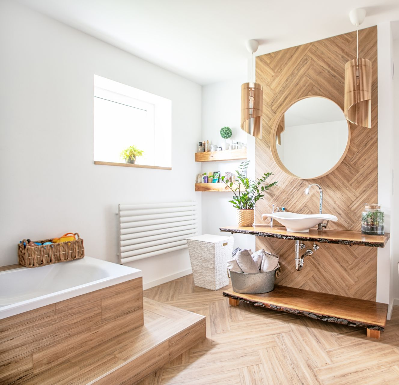 Une salle de bains moderne avec un mur d'accent en bois à chevrons, un meuble-lavabo en bois brut, un miroir rond et une baignoire encastrée.