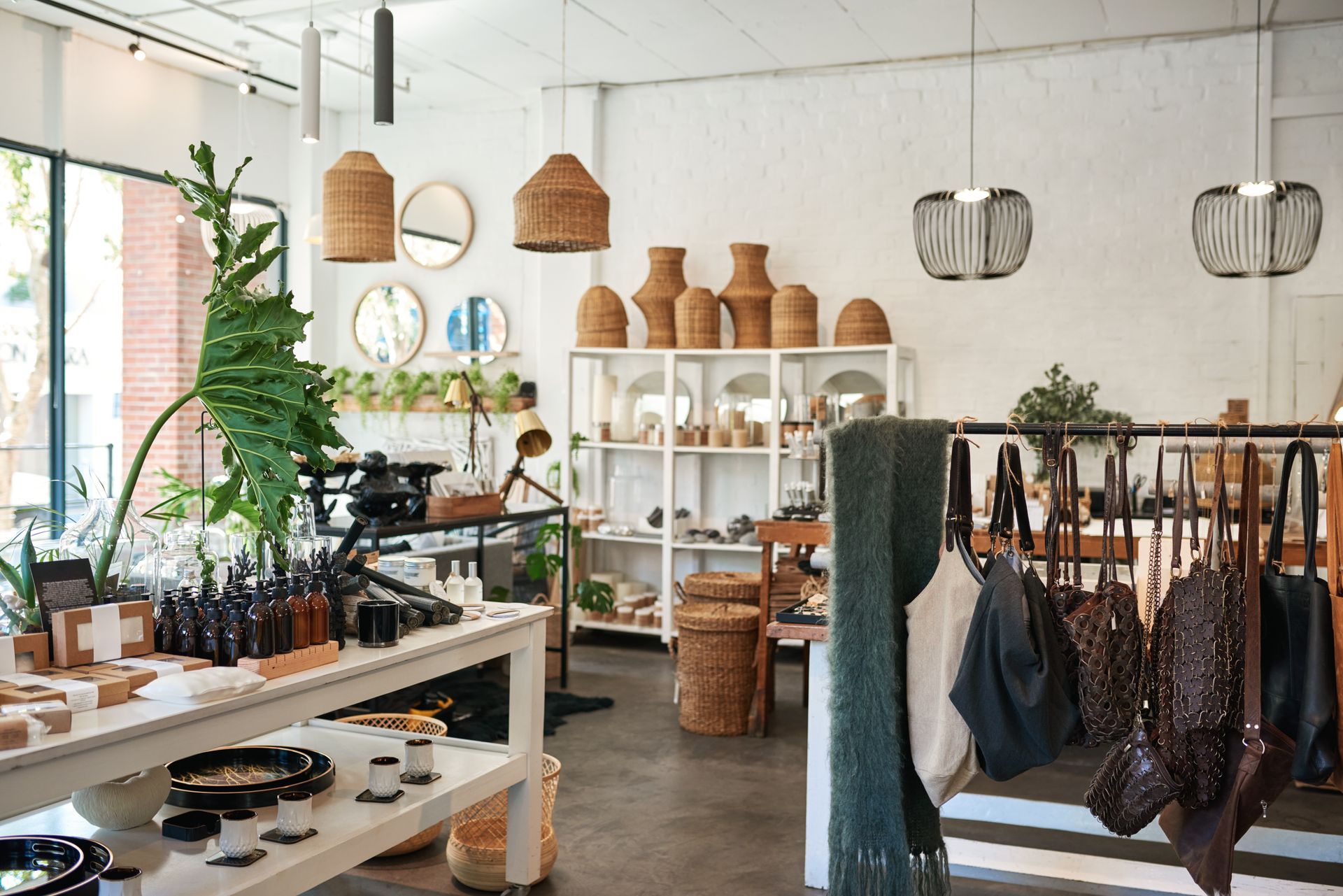 L'intérieur d'une boutique présente des tables avec des objets de décoration, des luminaires en osier, des étagères de céramiques et des sacs suspendus.