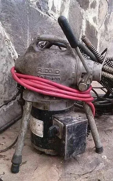 Un limpiador de desagües está sentado en el suelo al lado de una pared.