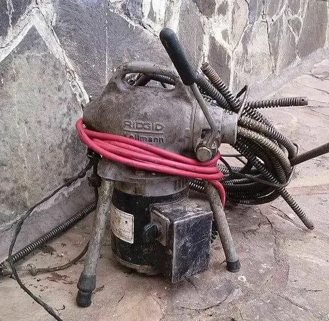 Un limpiador de desagües está sentado en el suelo al lado de una pared.