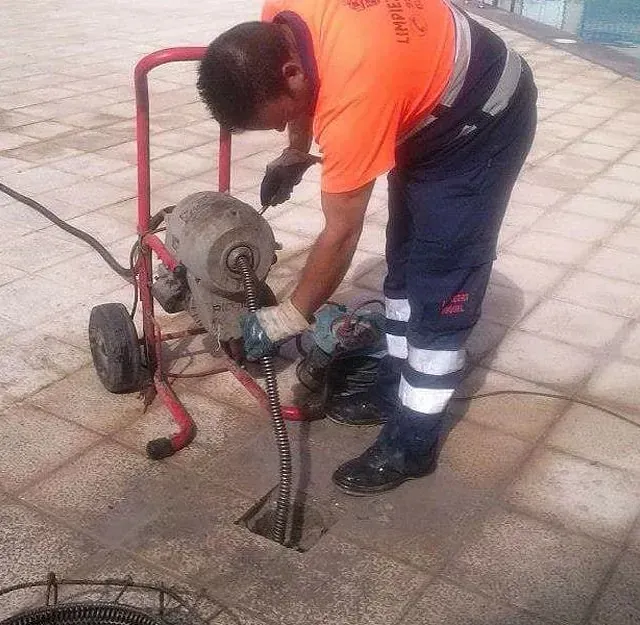Un hombre con una camisa naranja está usando una máquina para limpiar un desagüe.