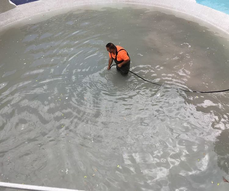 Un hombre con un chaleco naranja está arrodillado en una piscina.