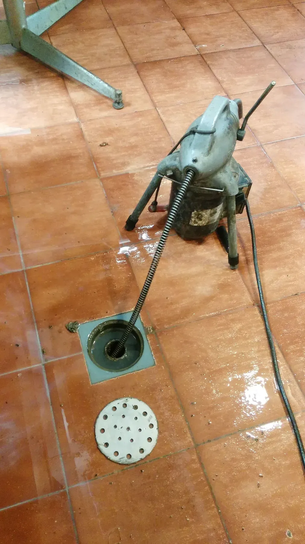 Una máquina está colocada sobre un suelo de baldosas junto a un desagüe.