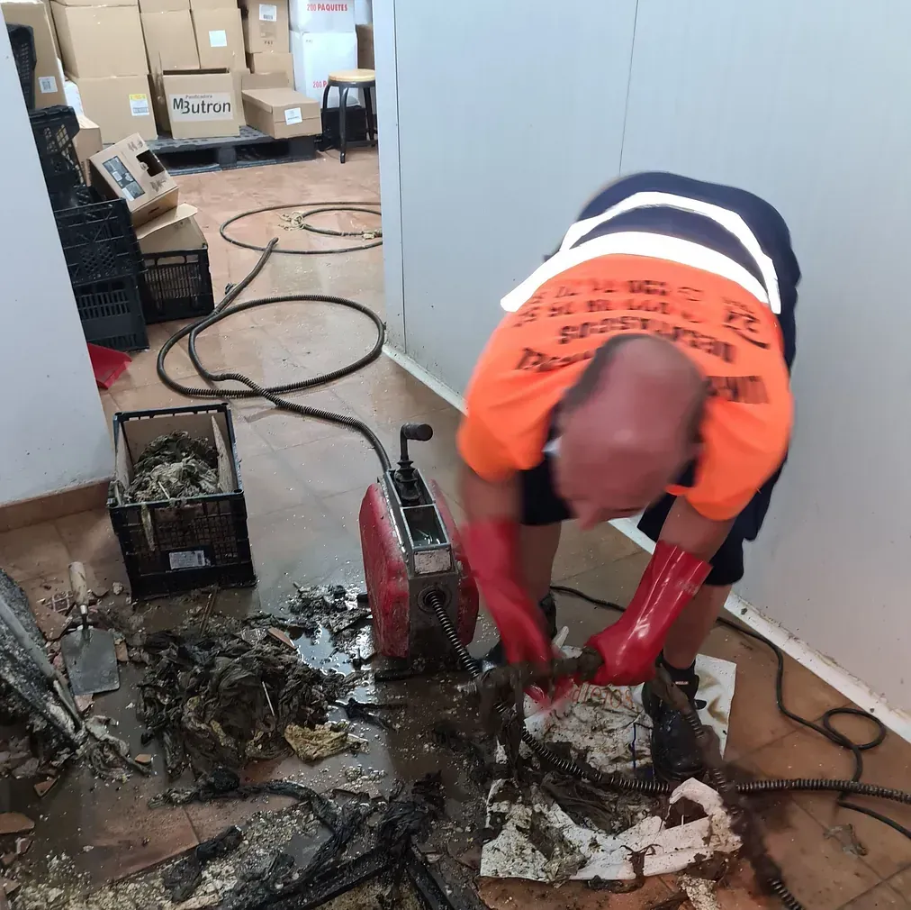 Un hombre con una camisa naranja está trabajando en un desagüe.