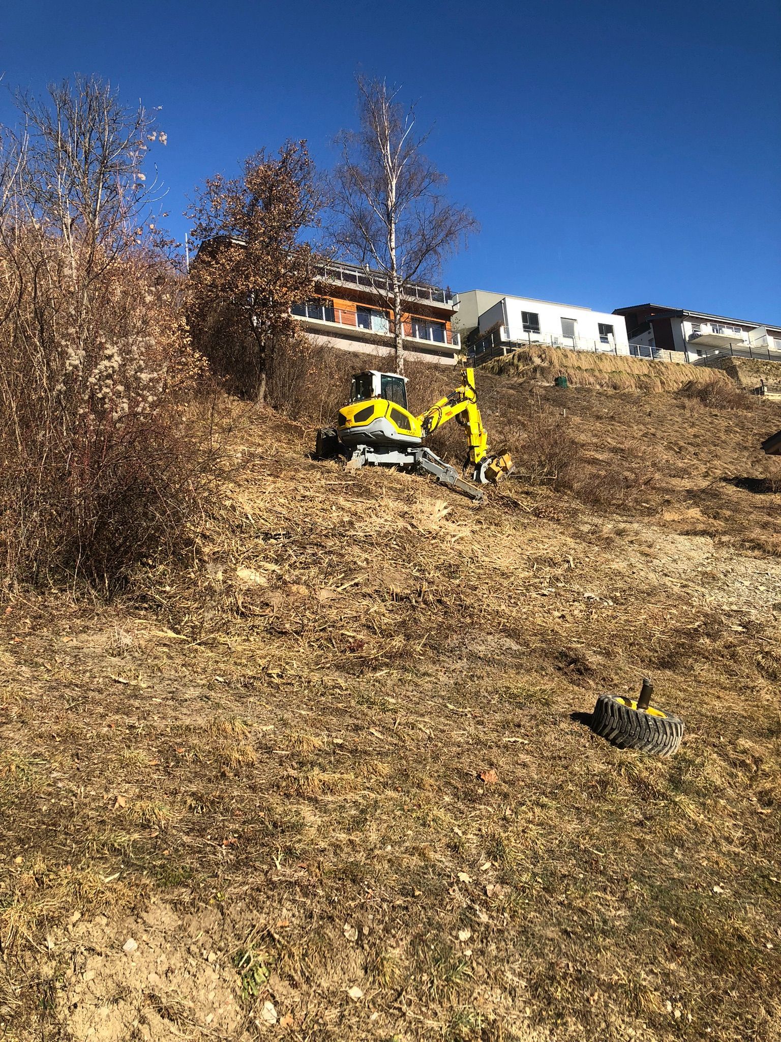 Une excavatrice jaune est assise au sommet d'une colline herbeuse sèche.