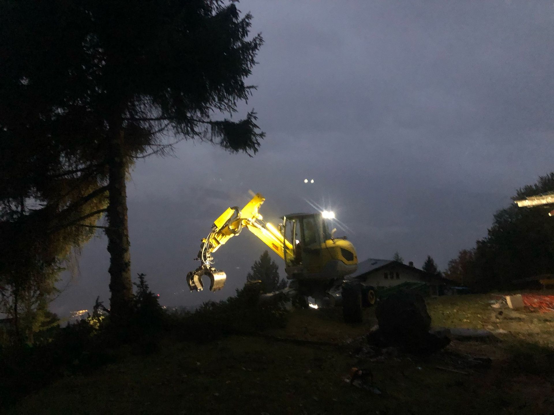 Une excavatrice jaune travaille dans le noir près d'un arbre.