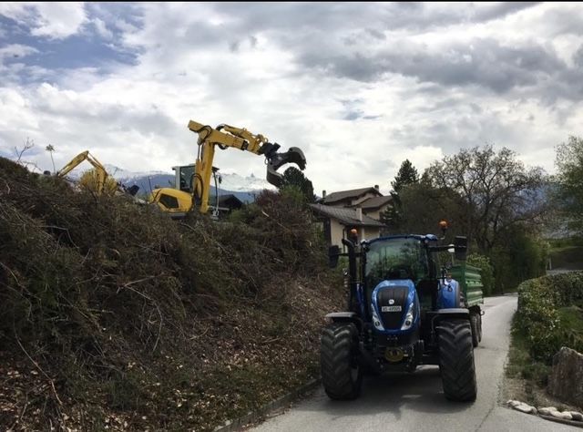 Un tracteur bleu roule sur une route à côté d'une excavatrice jaune.