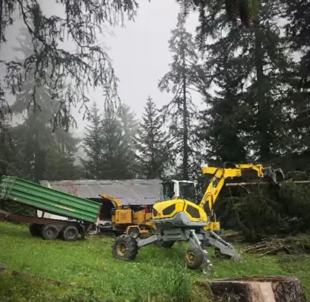 Une excavatrice jaune est garée dans un champ herbeux à côté d'un camion à benne basculante.