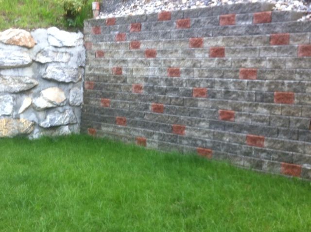 Un mur de briques est entouré de rochers et d'herbe dans une cour.