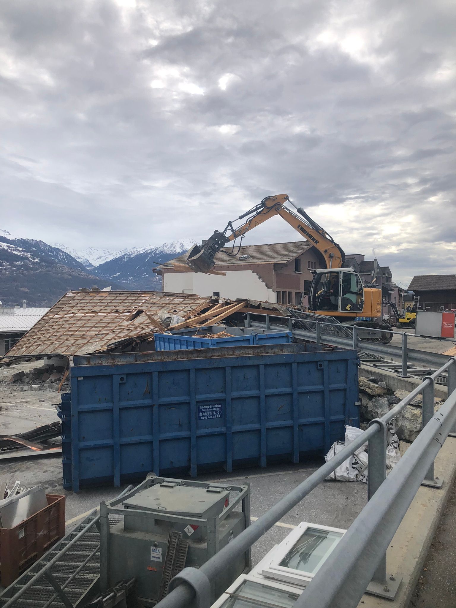 Une grande benne bleue se trouve devant un bâtiment en cours de démolition.