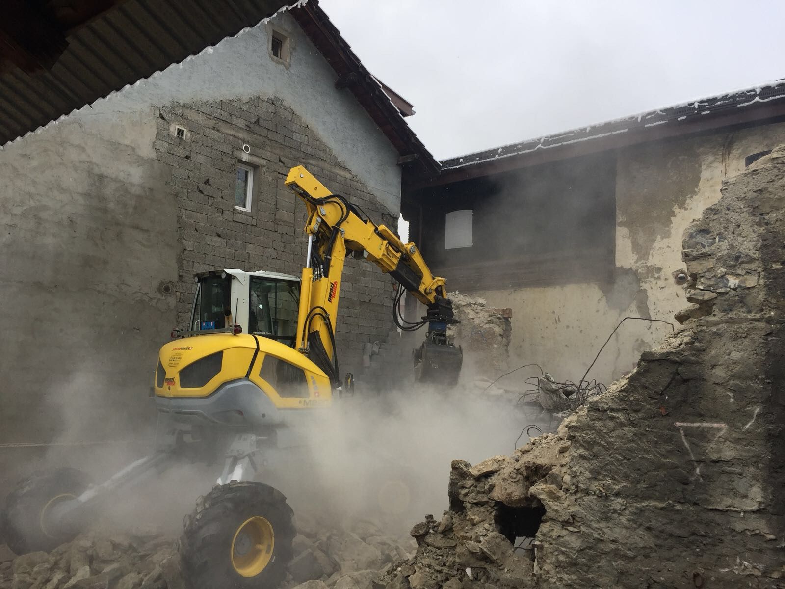 Une excavatrice jaune démolit un bâtiment en briques