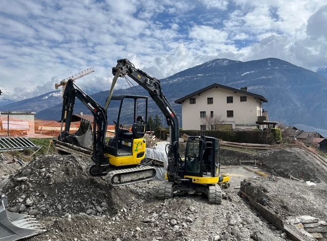Deux excavatrices travaillent sur un chantier de construction avec des montagnes en arrière-plan.