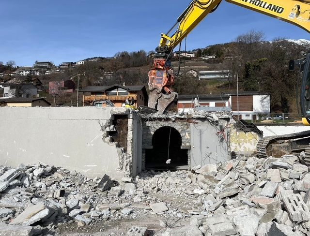 Une excavatrice jaune avec le mot Holland dessus démolit un bâtiment.