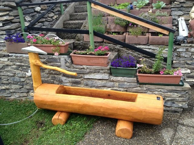 Une jardinière en bois en forme de canard se trouve devant un mur de pierre