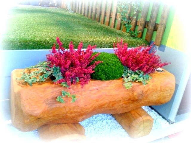 Une jardinière en bois remplie de fleurs et de mousse est posée devant une clôture.