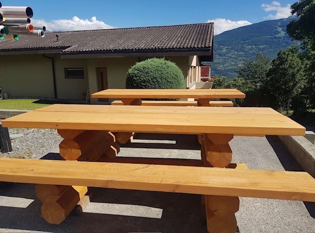 Une rangée de tables et de bancs en bois devant une maison