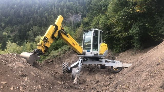 Une excavatrice jaune est assise au sommet d'une colline de terre.