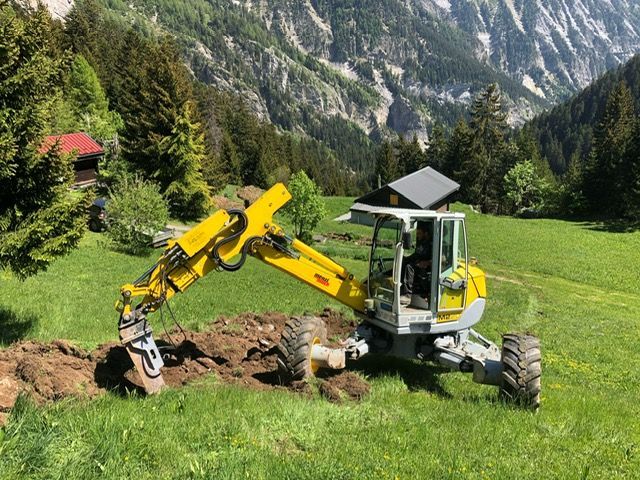 Une excavatrice jaune creuse un trou dans un champ herbeux.