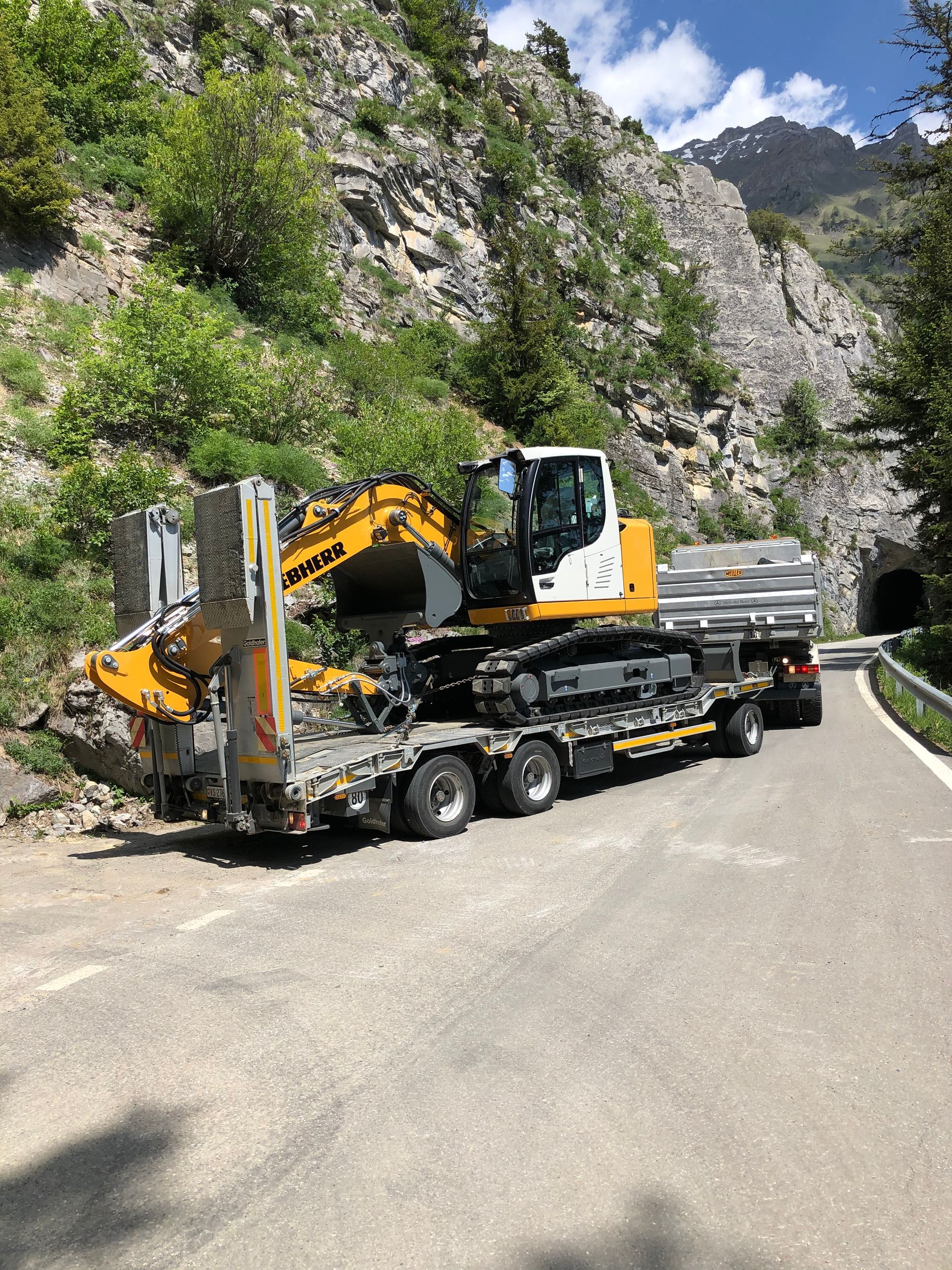 Une excavatrice jaune est assise sur une remorque sur une route.