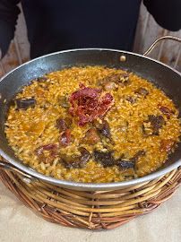 Un plato de arroz amarillo con trozos oscuros y guarnición, en una cesta de mimbre sobre una mesa.