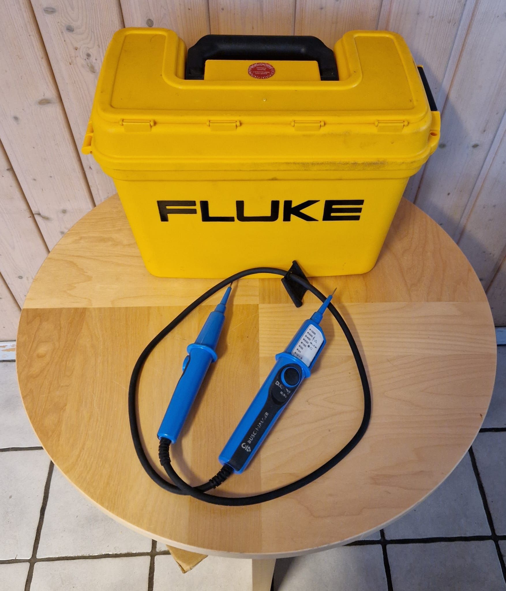 Gelber Fluke-Koffer und blauer Spannungsprüfer auf einem Holztisch.
