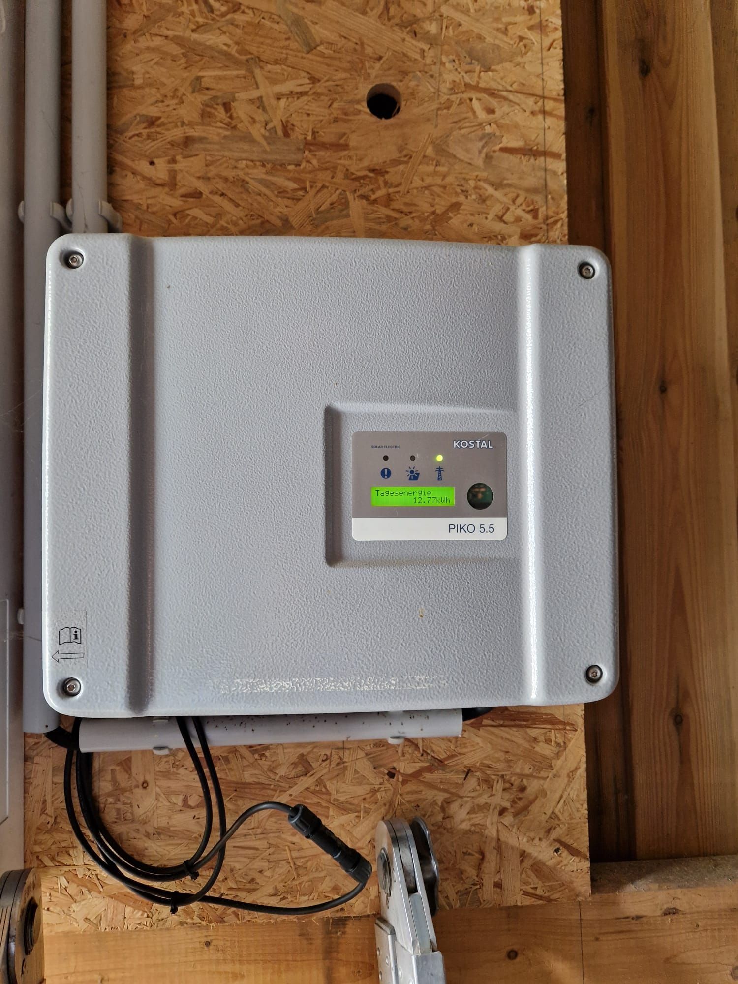 Grauer Solarwechselrichter auf Holzplatte montiert, mit beleuchteter Digitalanzeige.