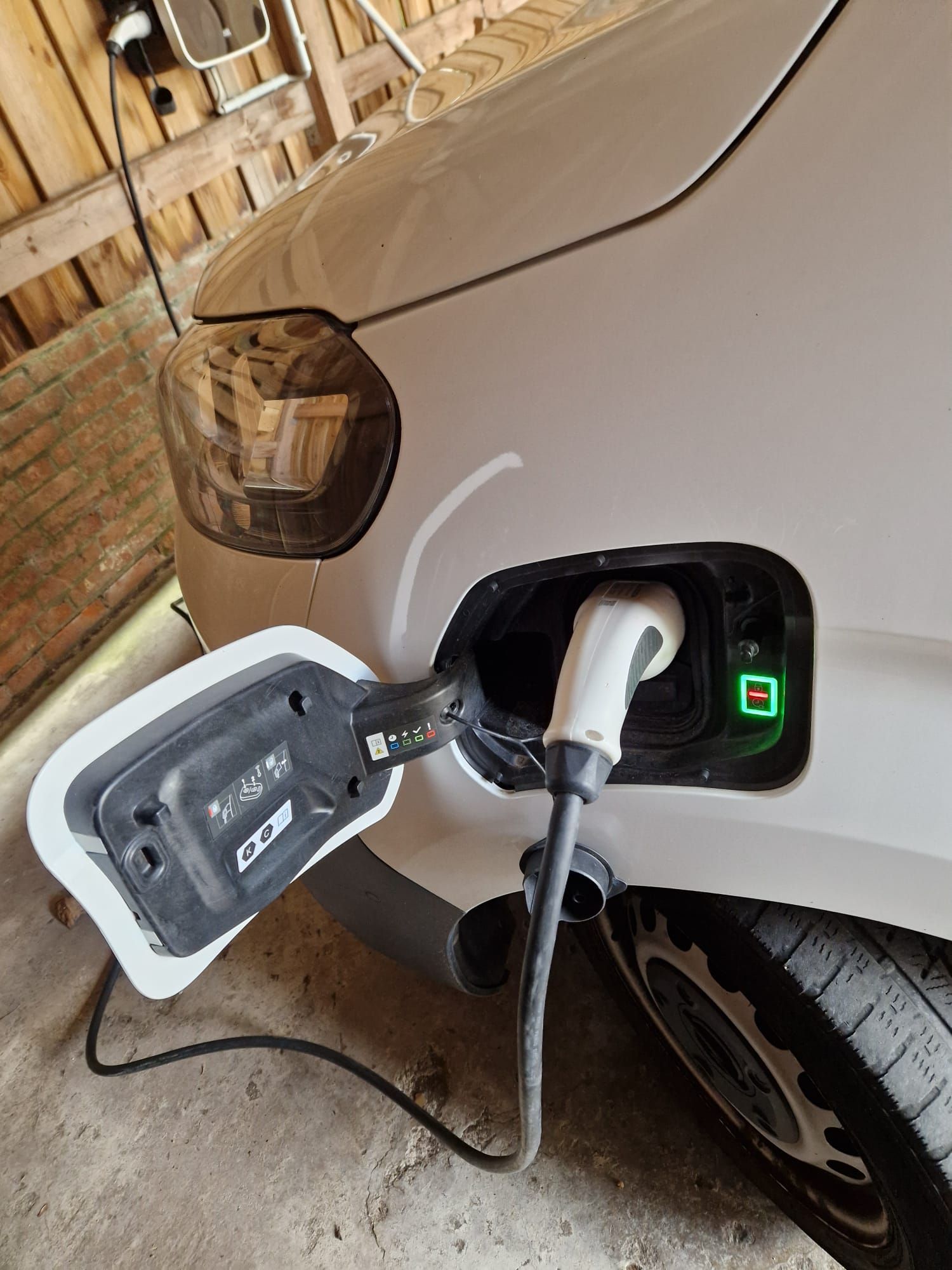 Weißes Elektroauto wird geladen, Kabel eingesteckt. Grünes Licht zeigt den Ladevorgang an.