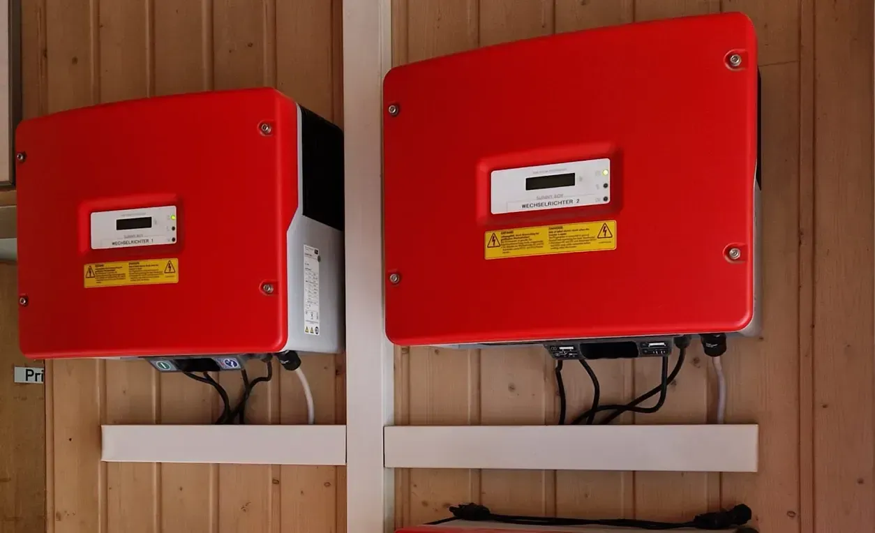 Zwei rote Solarwechselrichter, die an einer Holzwand montiert sind.